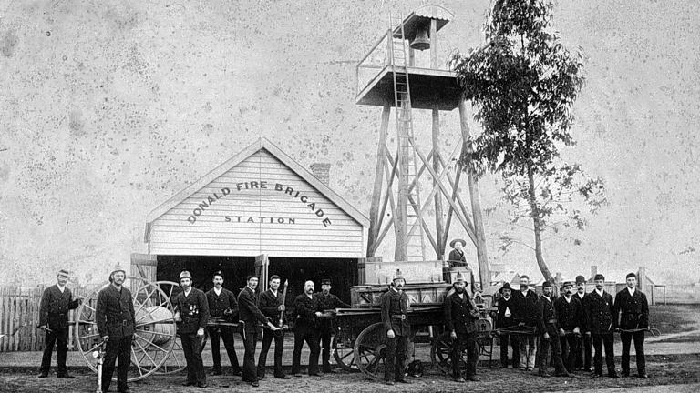 Black and white image of a group of firemen with equipment outside a building