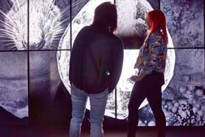 Two women in front of large video displays