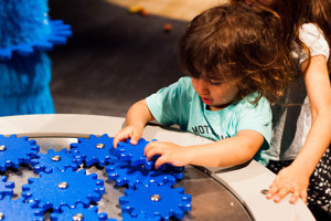Child playing with blue cogs in the Ground Up exhibition 