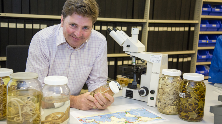 Dr. Tim O'Hara in Marine Vertebrate research laboratory holding a specimen jar containing Brittle Stars.