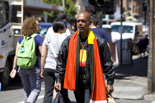 Man walking a long the street with an Aboriginal Flag draped over his shoulders