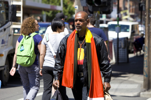 Man walking a long the street with an Aboriginal Flag draped over his shoulders