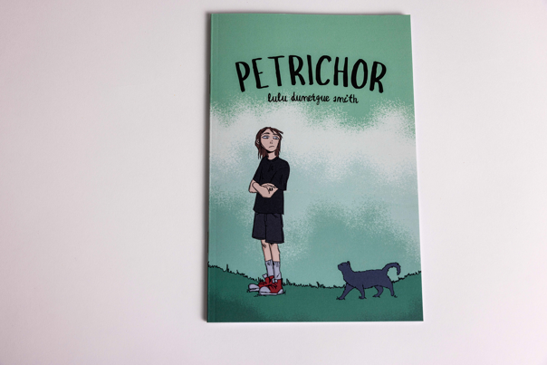 Illustrated book cover shows a young person with shoulder-length hair, wearing a black outfit and red sneakers, standing on grass with arms crossed. A cat walks nearby.