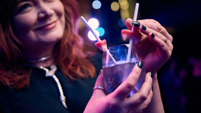 A woman wearing a witch costume holding a cocktail with candy teeth impaled on straws.