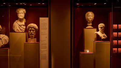 Display case of Roman marble busts arranged on plinths against deep red gallery walls in ROME: Empire, Power, People exhibition in Melbourne Museum.. 