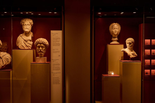 Display case of Roman marble busts arranged on plinths against deep red gallery walls in ROME: Empire, Power, People exhibition in Melbourne Museum.. 