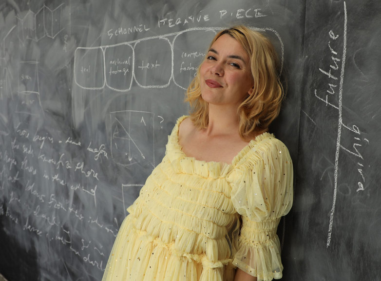 Jazz Money leans against a chalk board wearing a yellow summer dress.