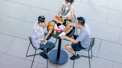 Three people sit at table and eat burgers and hotdogs