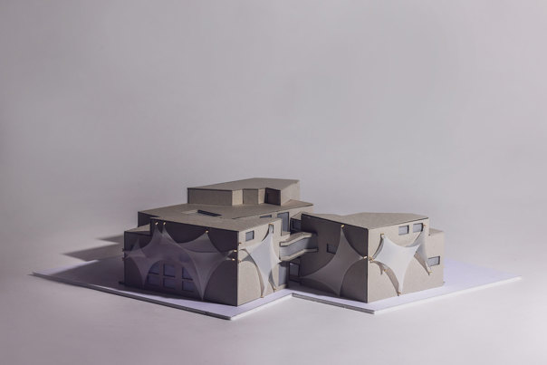 Architectural model of connected buildings with overlapping curved exterior panels and flat roofs in grey and white tones, mounted on a white base.