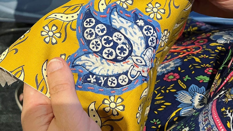 A person holding a piece of yellow floral fabric with a blue embroidery on it.