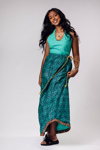 Person wears a turquoise sleeveless top with a patterned wrap skirt tied with a gold rope.