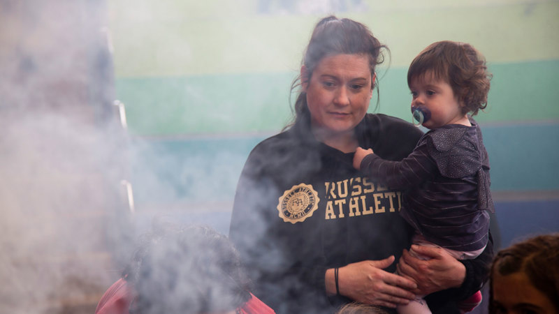 A baby in a woman's arms watch smoke during a smoking ceremony at Scienceworks.