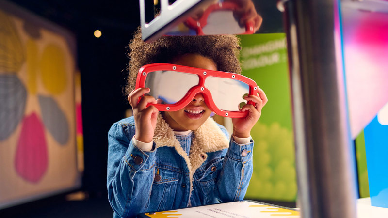 A child wearing large red glasses seeing light in an all new way at Colour exhibition, Scienceworks.