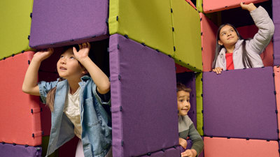 Children playing games in a cubby house they have built together out of multi-coloured cushions.