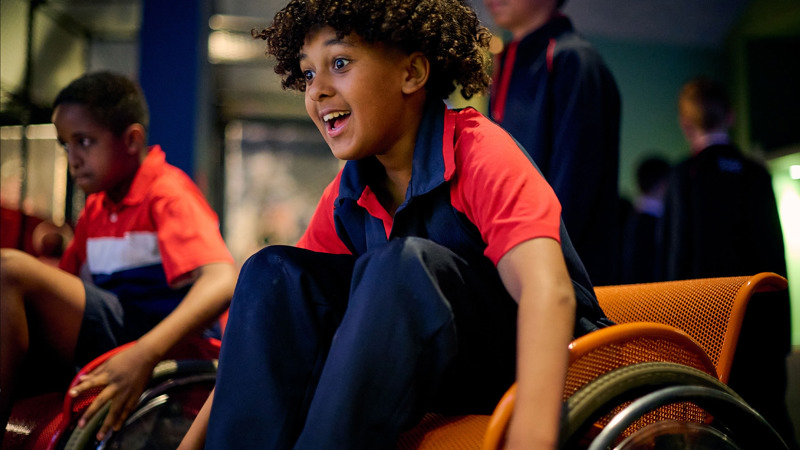 A primary school student excitedly participates in the wheelchair race in Sportsworks while on an excursion. 