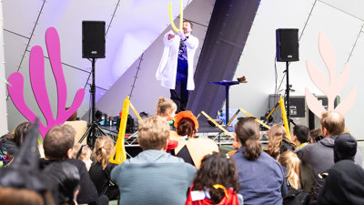 A man in a science lab coat entertains a crowd outside during Halloween at the Museum.