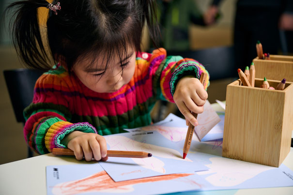 A small child colouring a post card to a dinosaur.
