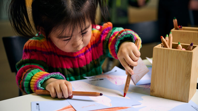 A small child colouring a post card to a dinosaur.