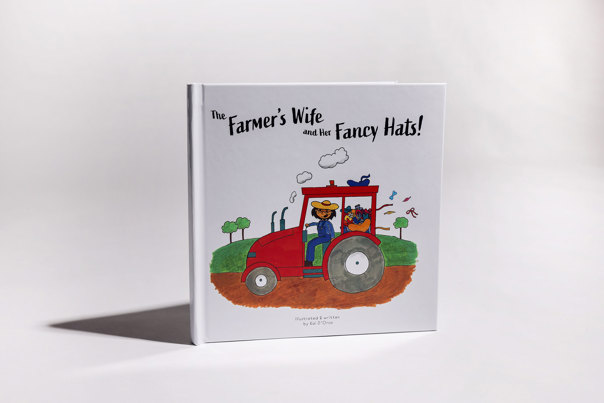 Picture book cover featuring a woman in overalls and a straw hat, driving a red tractor through a country landscape.