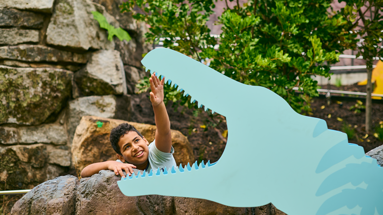 Child reaches for the mouth of a dinosaur in Gandel Gondwana Garden