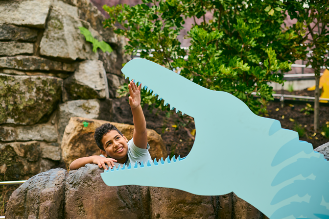 Child reaches for the mouth of a dinosaur in Gandel Gondwana Garden