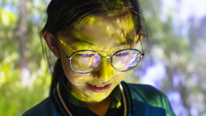 Student in immersive digital learning lab with leaves projected across her face. 
