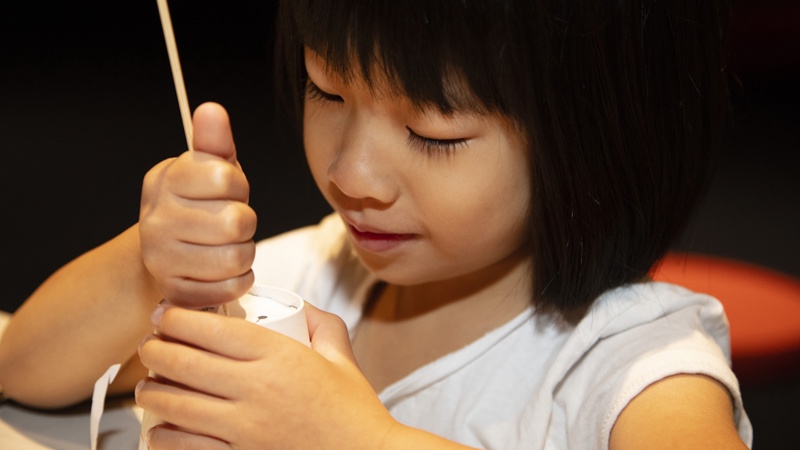 A young girl uses a skewer to poke holes in the top of her constellation cup
