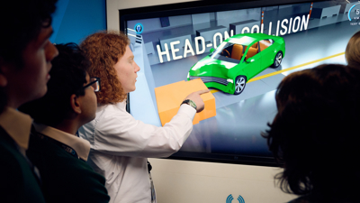 A group of students look at an interactive screen at an animation of a head-on collision simulation.