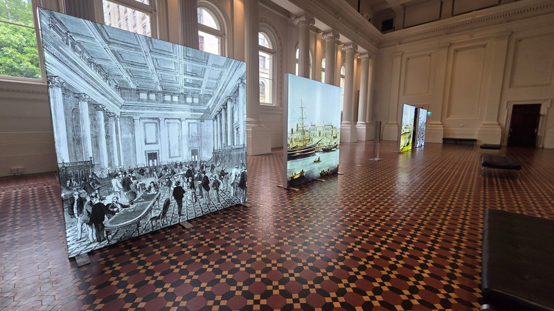 Illuminated images of early Melbourne standing on the floor of the Long Room in the Immigration Museum.