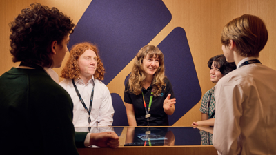 A group of students and a learning facilitator in the Road to Zero Learning Studio standing and sitting around a touch table 