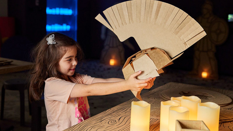 A young girl holds a Centurion helmet she has made herself from cardboard.