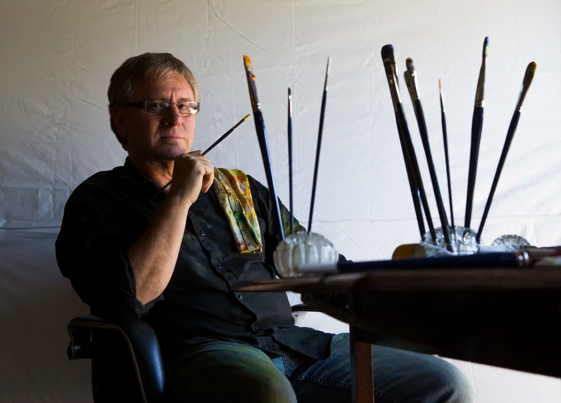 Richard Payne sits next to paints and brushes.
