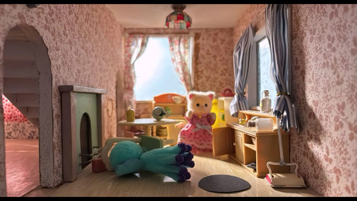 Stop-motion animation scene showing a miniature bedroom with floral wallpaper. A white cat figure wearing a pink dress can be seen amid furniture in disarray.