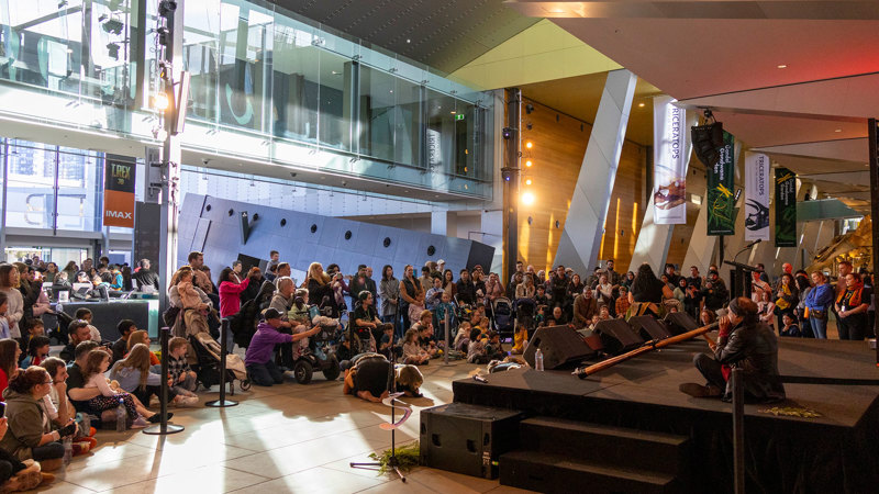 Amos Roach and the Murrundaya Yepenga Dance Troupe performing to a large audience during the Family Day event for NAIDOC Week held at Melbourne Museum. 