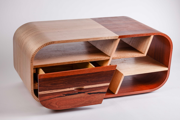 Rectangular coffee table in mixed wood tones with curved edges, enclosed sides and open compartments segmented by angled dividers. One front drawer is partially opened.
