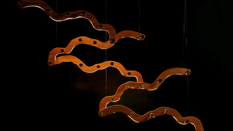 Suspended light feature with sculptural, undulating wood components.