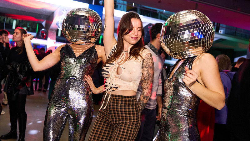 People dancing with two women wearing disco balls on their heads at Discoteca Italiana, Melbourne Museum.