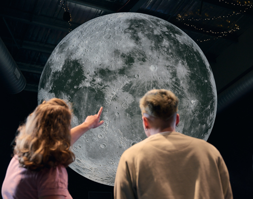 People pointing at the four metre wide moon installation in the planetarium at Scienceworks.