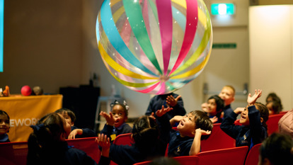  Primary school aged girl squeezing a pig toy in front of her with a ball that is about to pop out with Scienceworks staff member helping hold the toy stable.