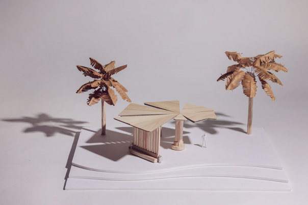 Architectural model of a shade pavilion with triangular roof panels in natural wood, supported by vertical slats, flanked by two stylised palm trees, mounted on a white base.