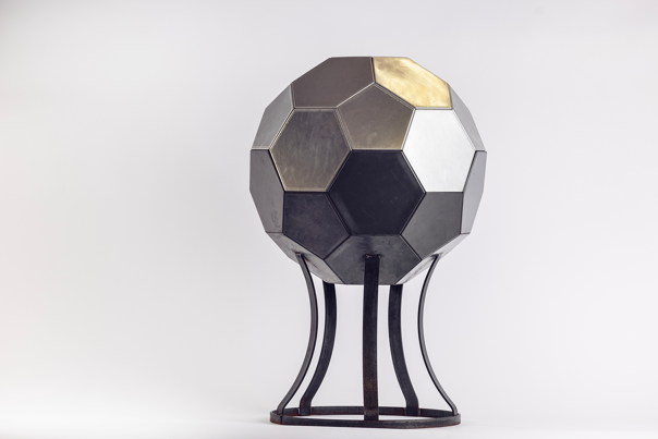 Geodesic metal sphere with hexagonal panels in dark tones, resting on a curved black-metal stand.