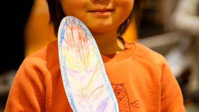 A small child holding a coloured in Bunjil's feather from a crafting activity during Little Kid's Day In.