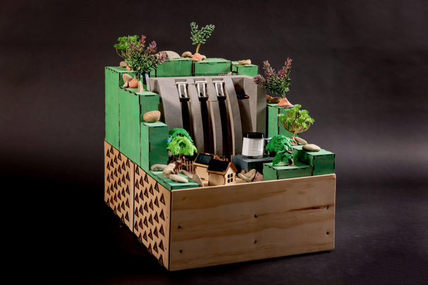 Model of a dam, featuring trees and rocks and sitting atop a large wooden base.