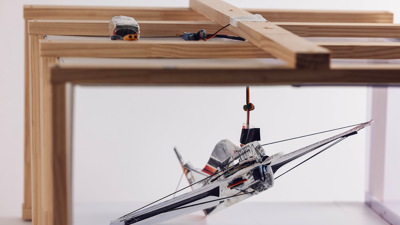 Model aeroplane suspended under a wooden frame with attached wiring and motors.