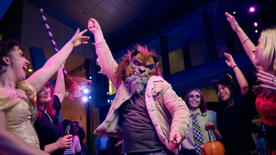 A man dressed as American teen wolf surrounded by people dressed as a vampire, a witch, zombies and cat on the dancefloor.