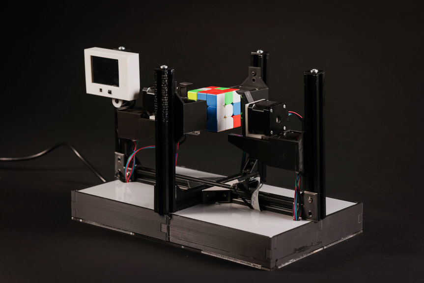 A Rubik’s Cube held up by black stepper motors affixed to a silver rectangular base. 