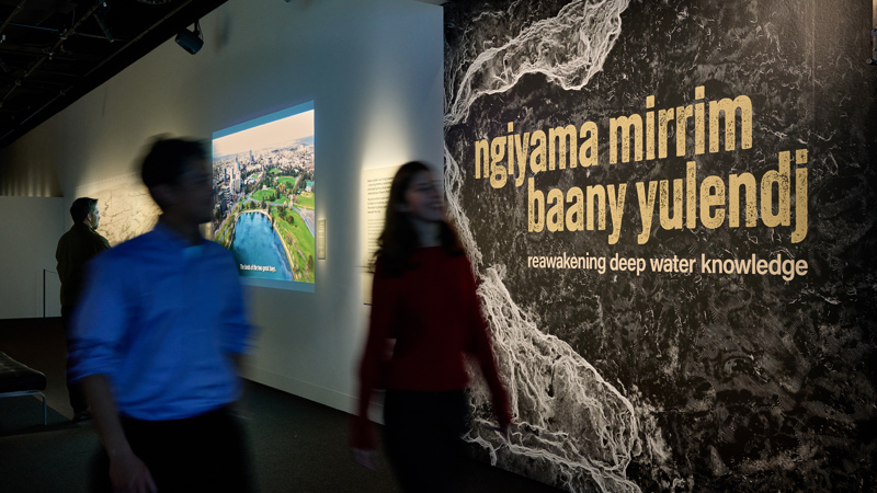 two Museum visitors walking past the entry to ngiyama mirrim baany yulendj | reawakening deep water knowledge exhibition.