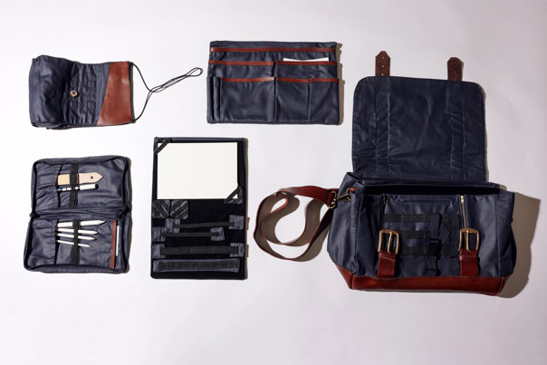 Flat lay of a navy blue and brown-leather artist's bag with its compartments and organisers displayed, including brush rolls, tool pouches, and a portable easel.