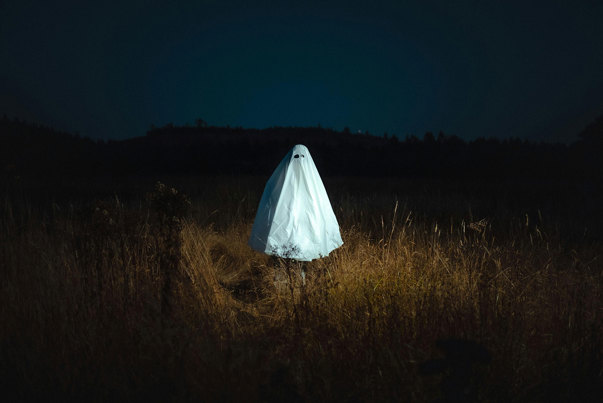 A person wearing a sheet to look like a ghost standing in a field at night.