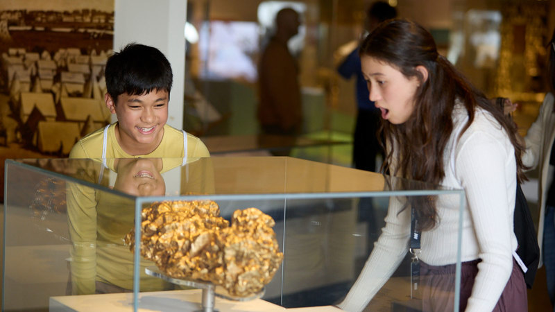Teenage siblings looking at a replica of a large gold nugget in a display case.